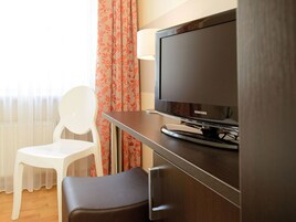 A hotel room with a television on a wooden stand, a white chair, and a small table.