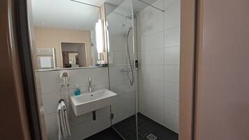 Un baño moderno con cabina de ducha de vidrio, un lavabo con espejo y un perchero para toallas.