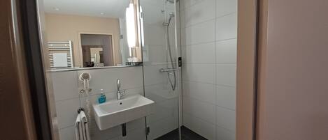 Un baño moderno con cabina de ducha de vidrio, un lavabo con espejo y un perchero para toallas.