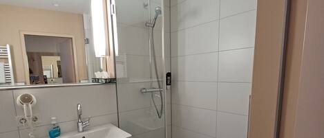Un baño moderno con ducha envuelta en vidrio, un lavamanos blanco y un espejo.