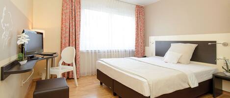 A hotel room with a bed, a desk with a computer, a chair, and a small table.