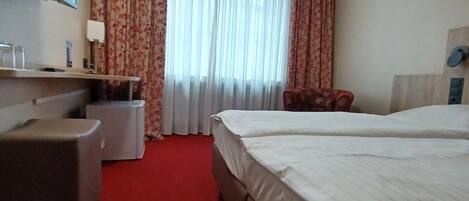 A hotel room with a large bed, a small desk, a chair, and a television on the wall.