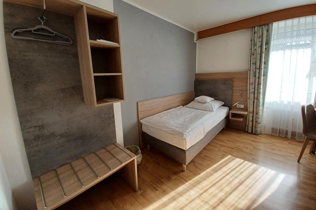 A bedroom with a bed, a wooden bench, a bedside table, and a hanging shelf with a hanger.