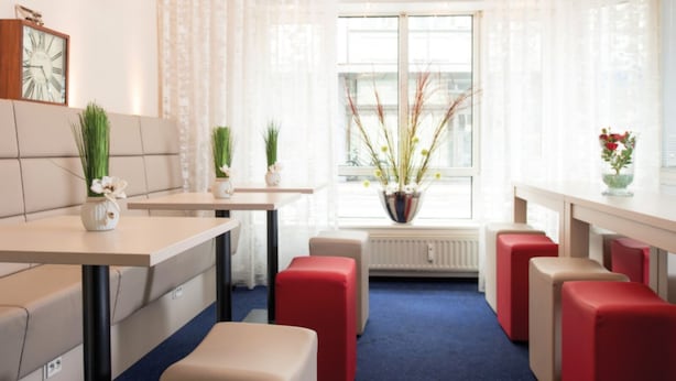 A modern hotel room with a dining area, red cushioned seating, a large window with curtains, and a radiator. - Hotel Europa (Bonn)