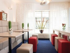 A modern hotel room with a dining area, red cushioned seating, a large window with curtains, and a radiator.