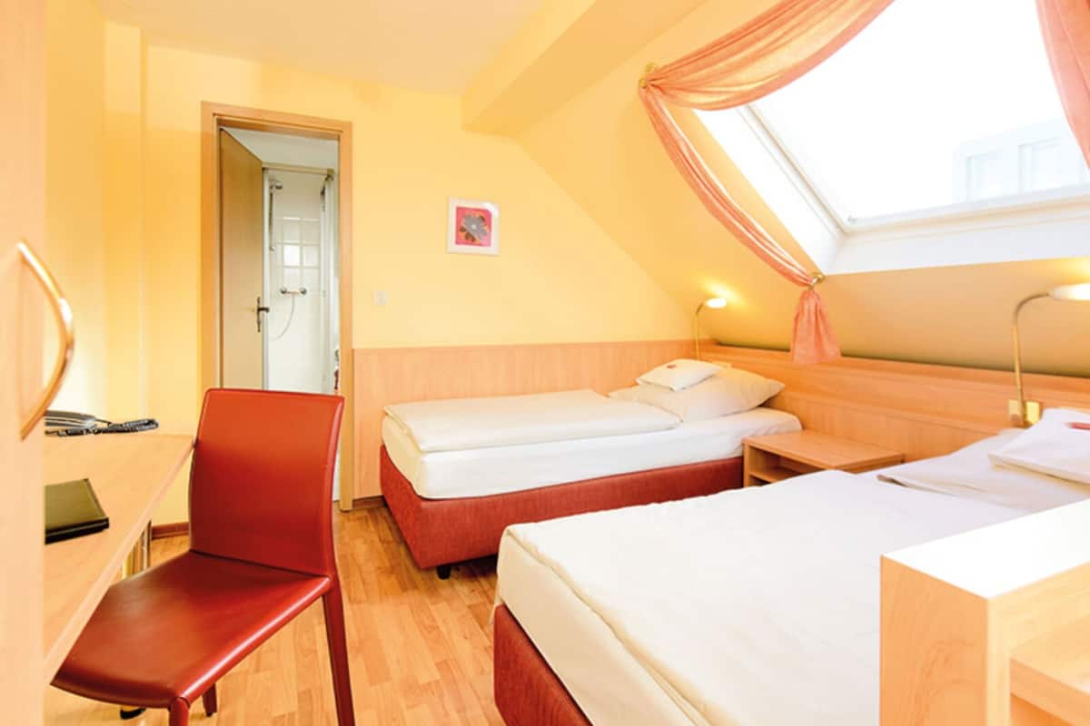 A hotel room with two beds, a desk, a chair, and a shower area.