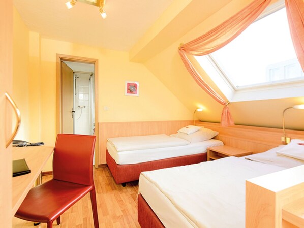 Habitación de hotel con dos camas, un escritorio, una silla y zona de ducha.