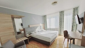 A modern hotel room with a bed, a desk, a chair, a small table, and a mirror. - Hotel Europa (Bonn)