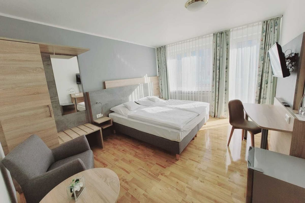 A modern hotel room with a bed, a desk, a chair, a small table, and a mirror.