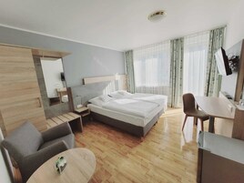 A modern hotel room with a bed, a desk, a chair, a small table, and a mirror.