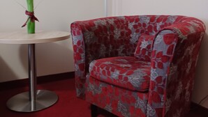 A corner room with a red carpet, a floral-patterned armchair, a small round table, and a white floor lamp. - Hotel Europa (Bonn)