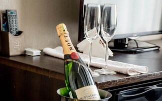 A bottle of Moët & Chandon champagne in a bucket, two empty champagne glasses, a remote control, and a smartphone on a wooden table.