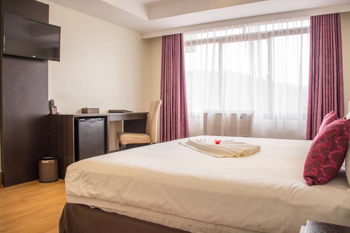 A hotel room with a bed, a desk, a chair, and a TV.