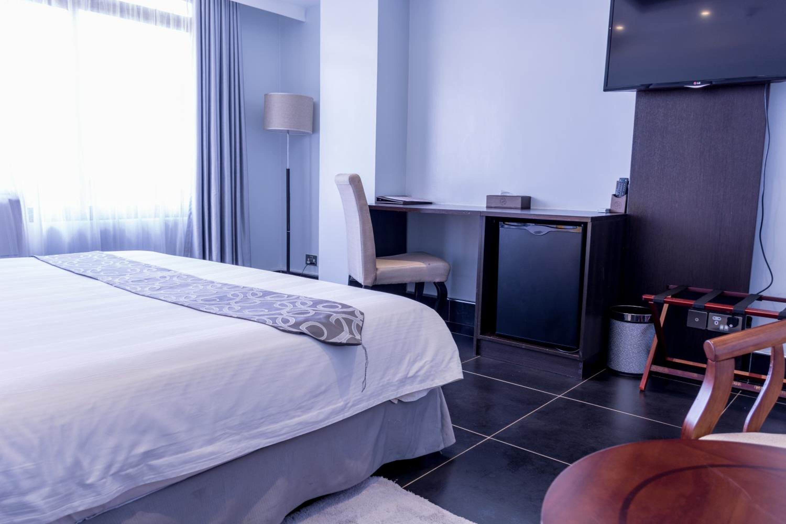 Una habitación de hotel moderna con una cama grande, un escritorio, una silla, un televisor y un bote de basura.