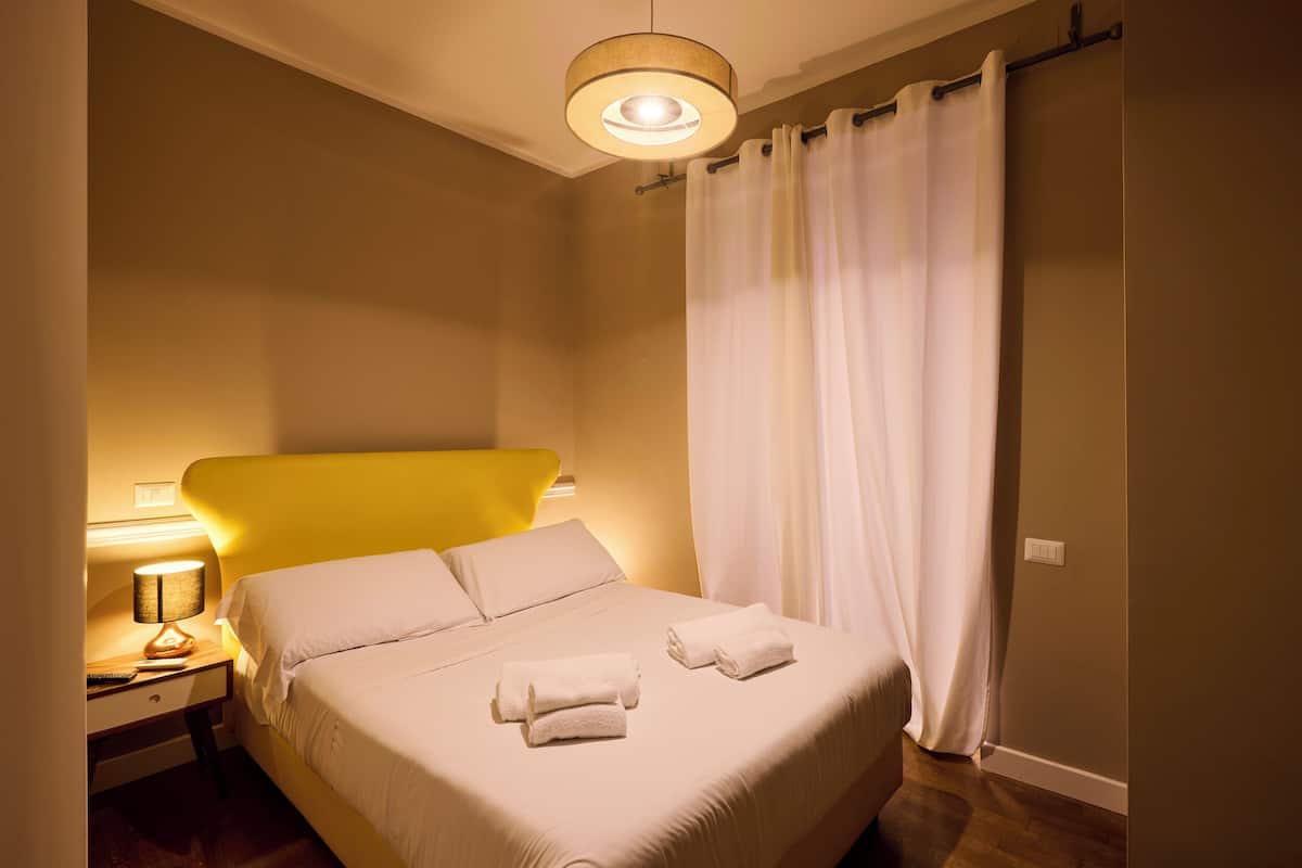 Une chambre d’hôtel avec un lit, une table de chevet avec une lampe et un rideau.