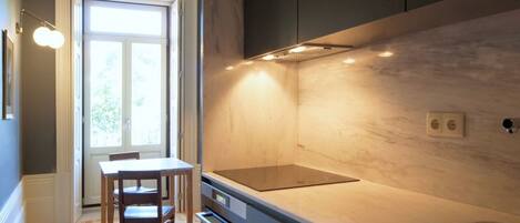 A modern kitchen with a built-in stove, a window, and a dining area with a table and chairs.