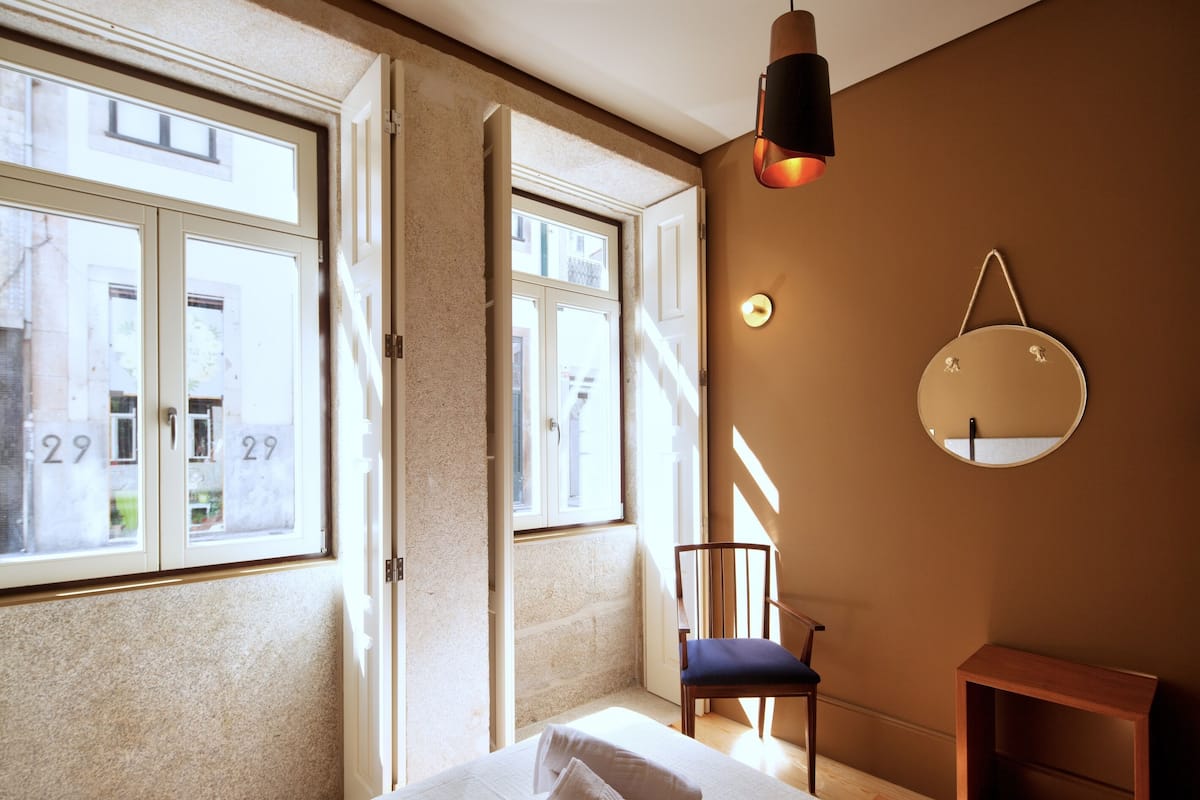 Une chambre à coucher avec un grand lit, une chaise, une petite table et un miroir fixé au mur.