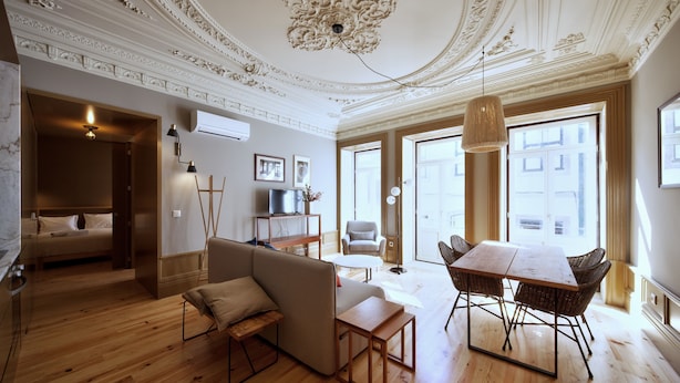 Een ruime kamer met houten vloer, een bank, een eettafel met stoelen, een televisie en een plafond met gedetailleerde decoraties.