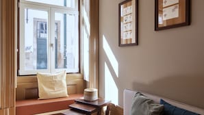 Een kamer met een groot raam, een bank, een klein tafeltje en ingelijste foto’s aan de muur.