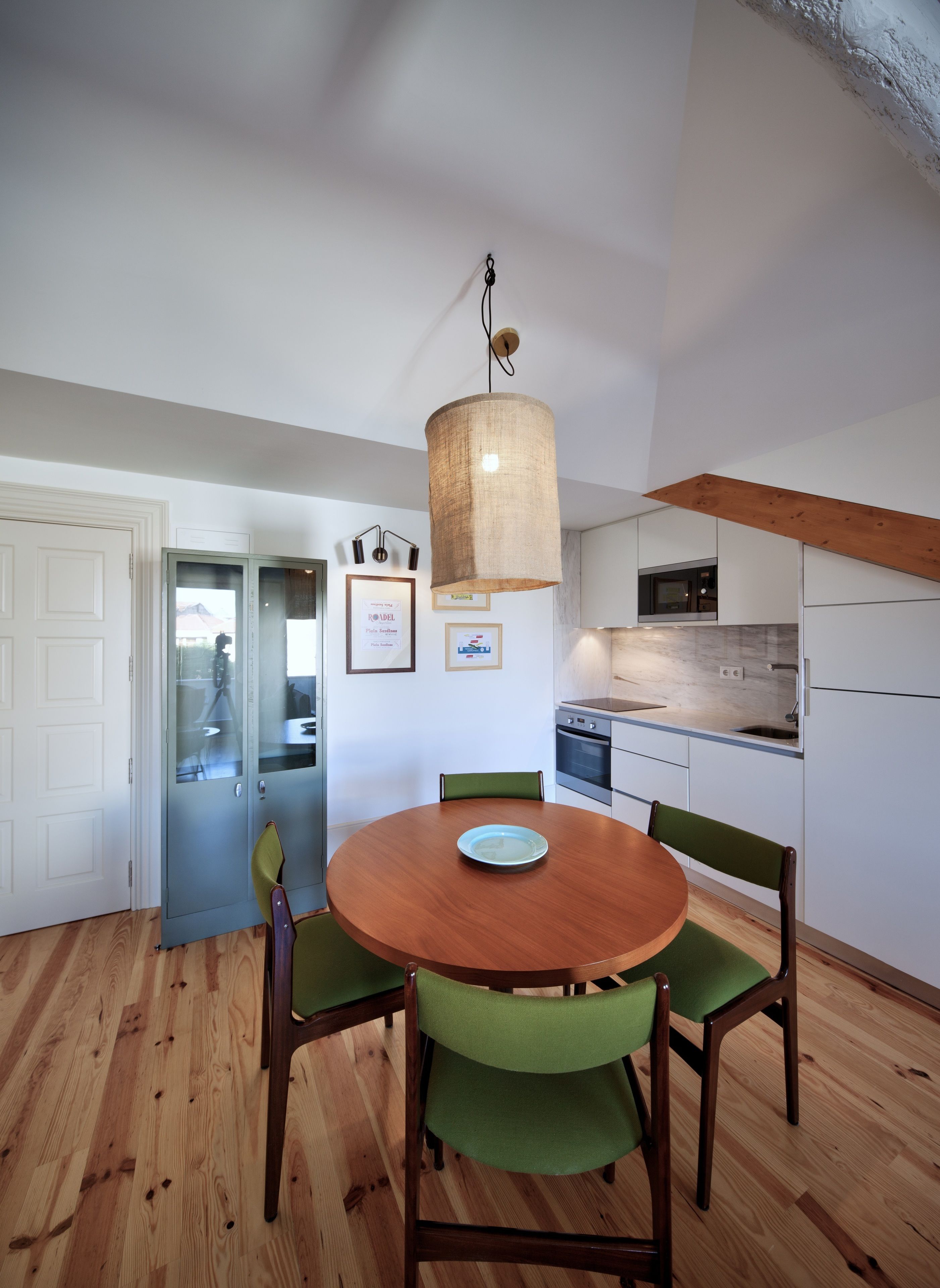 Een moderne keuken met witte kasten, een houten eettafel met vier stoelen, en een hangende lamp.