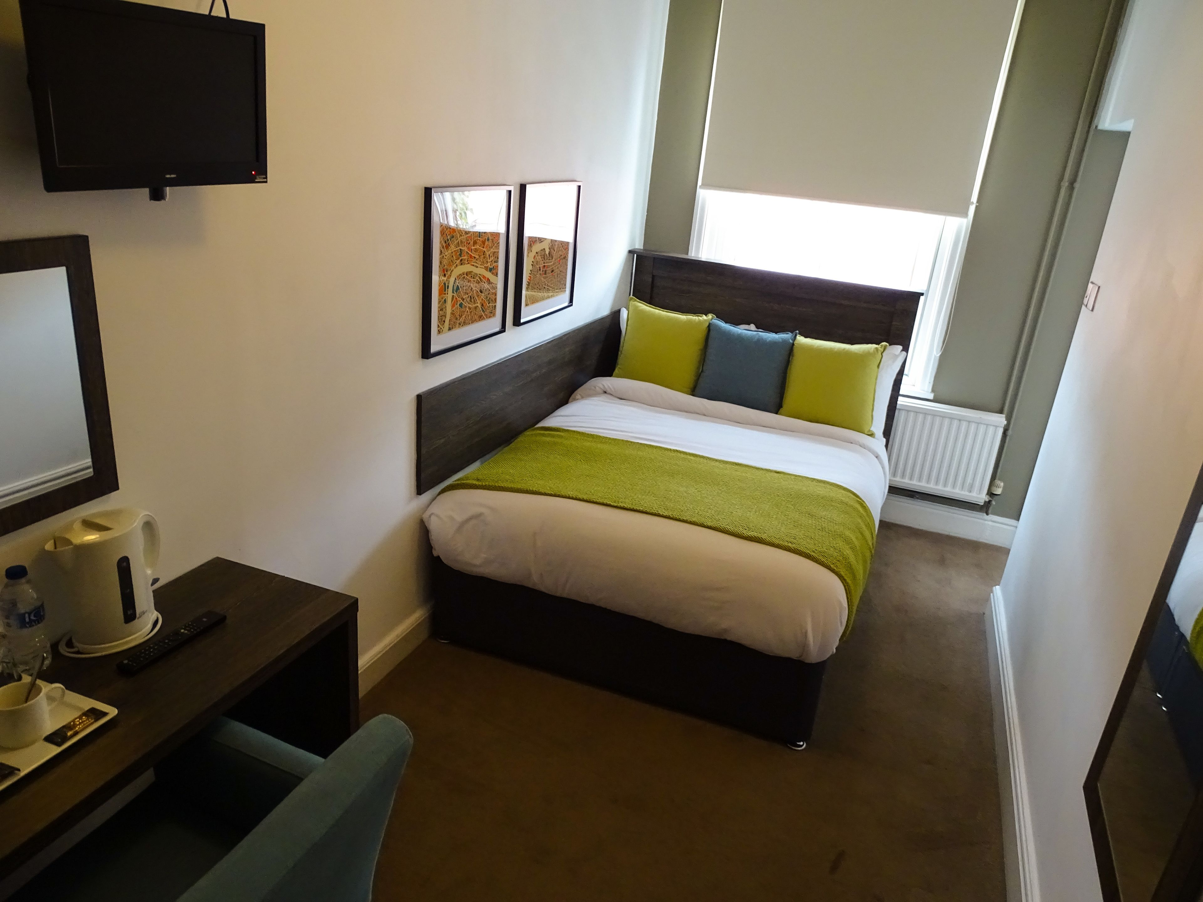 Habitación de hotel con cama, escritorio con cafetera, televisión y obras de arte en la pared.