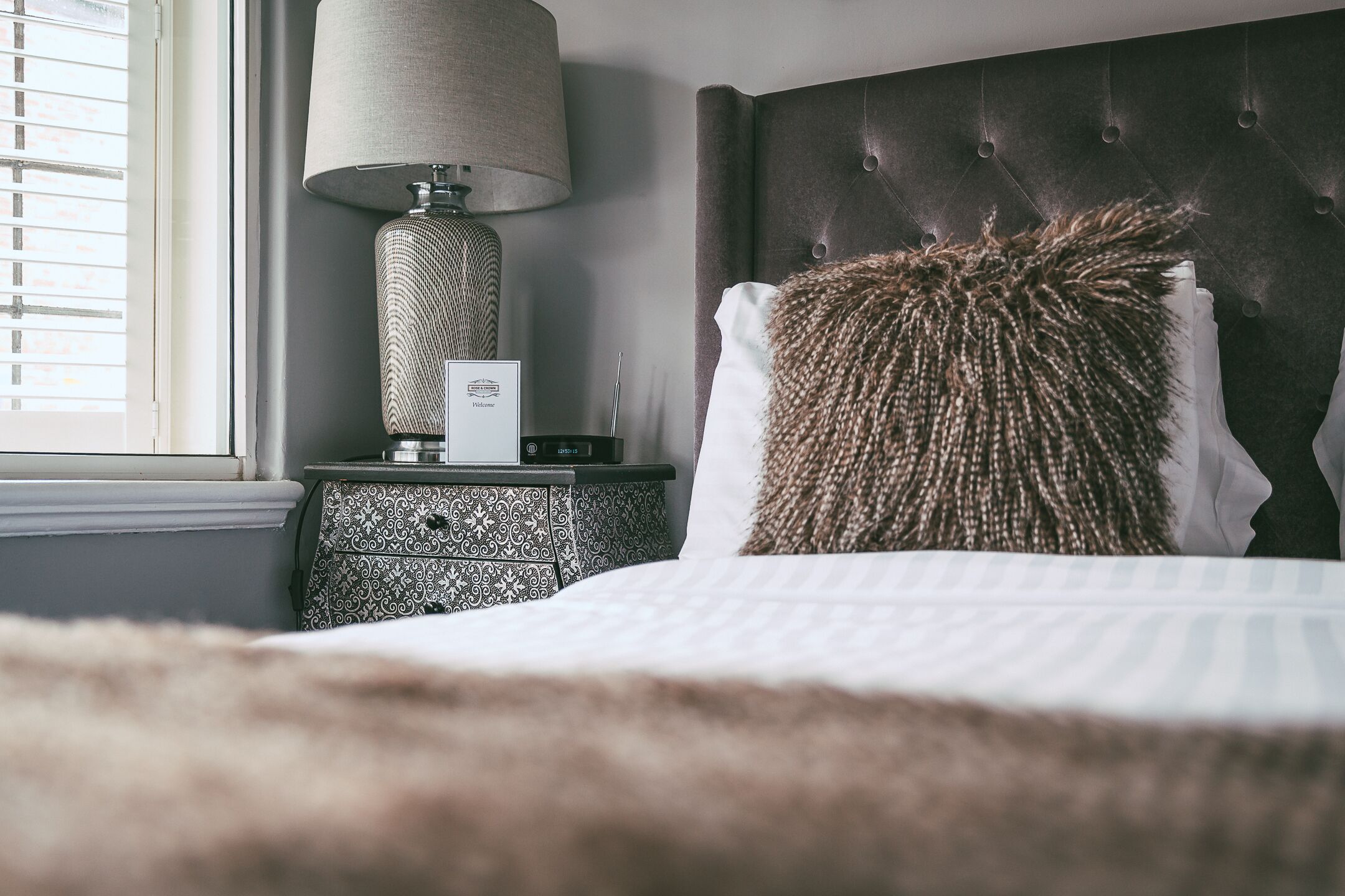 Una cama bien hecha con un almohadón mullido, una lámpara de noche y una mesita de noche con diseño.
