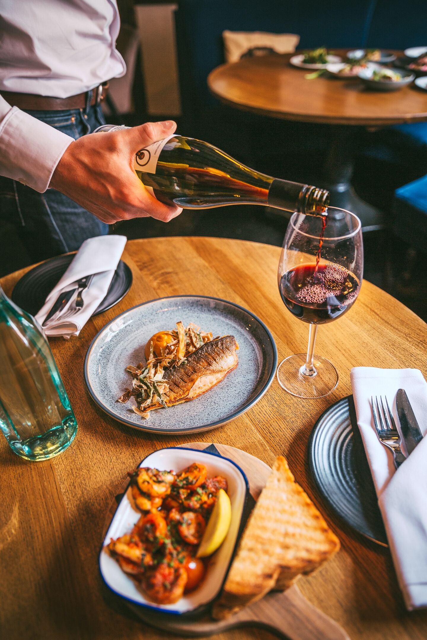 A dining table with a plate of food, a glass of red wine, and a bottle of water.