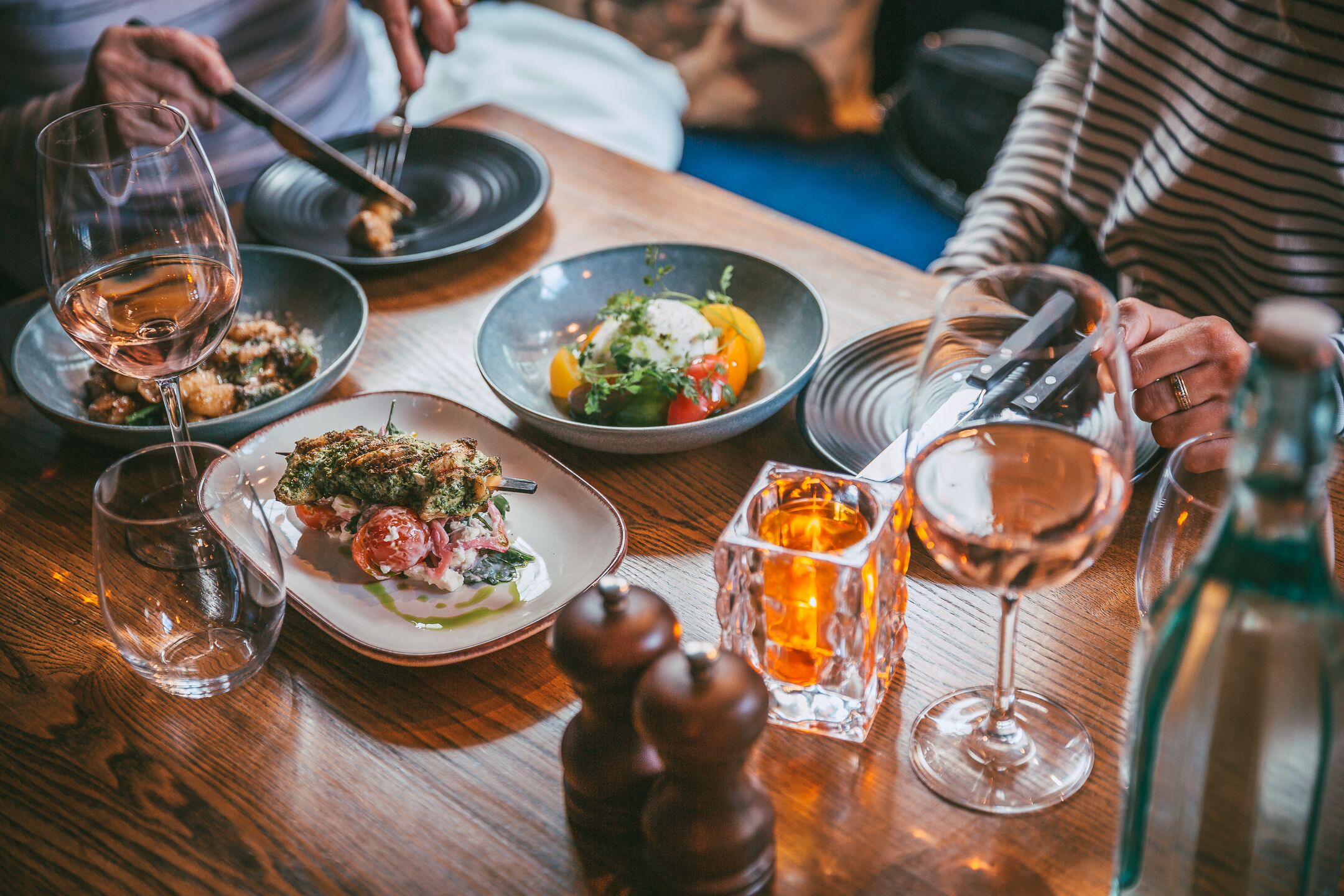 A dining table with plates of food, glasses of wine, and a candle.
