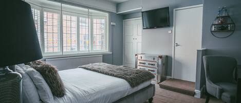 A bedroom with a large bed, a television mounted on the wall, a dresser, and a chair.