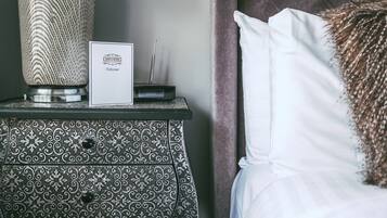 A neatly made bed with white linens and a decorative pillow, a patterned vase, and a framed welcome sign on a bedside table.