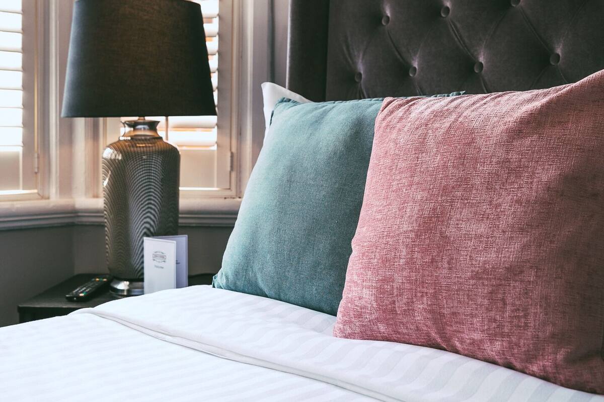 Un letto rifatto con cura, con lenzuola a righe, una testiera scura capitonata e due cuscini color verde acqua e rosa.