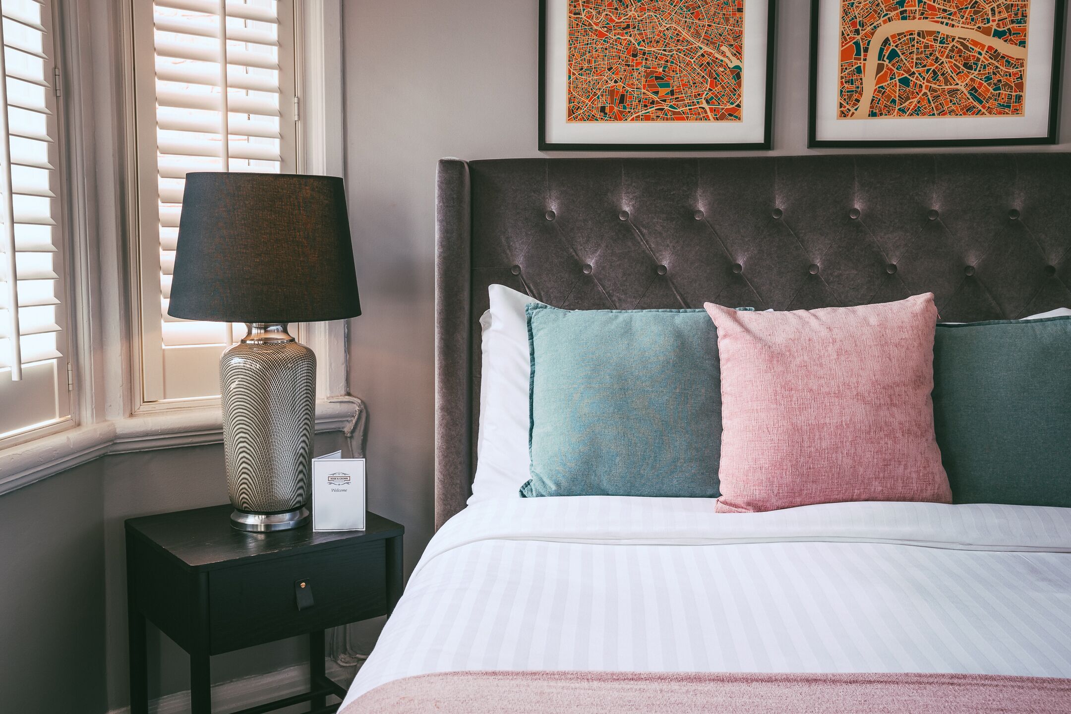 A neatly made bed with a tufted headboard, a bedside lamp, and two framed artworks on the wall.