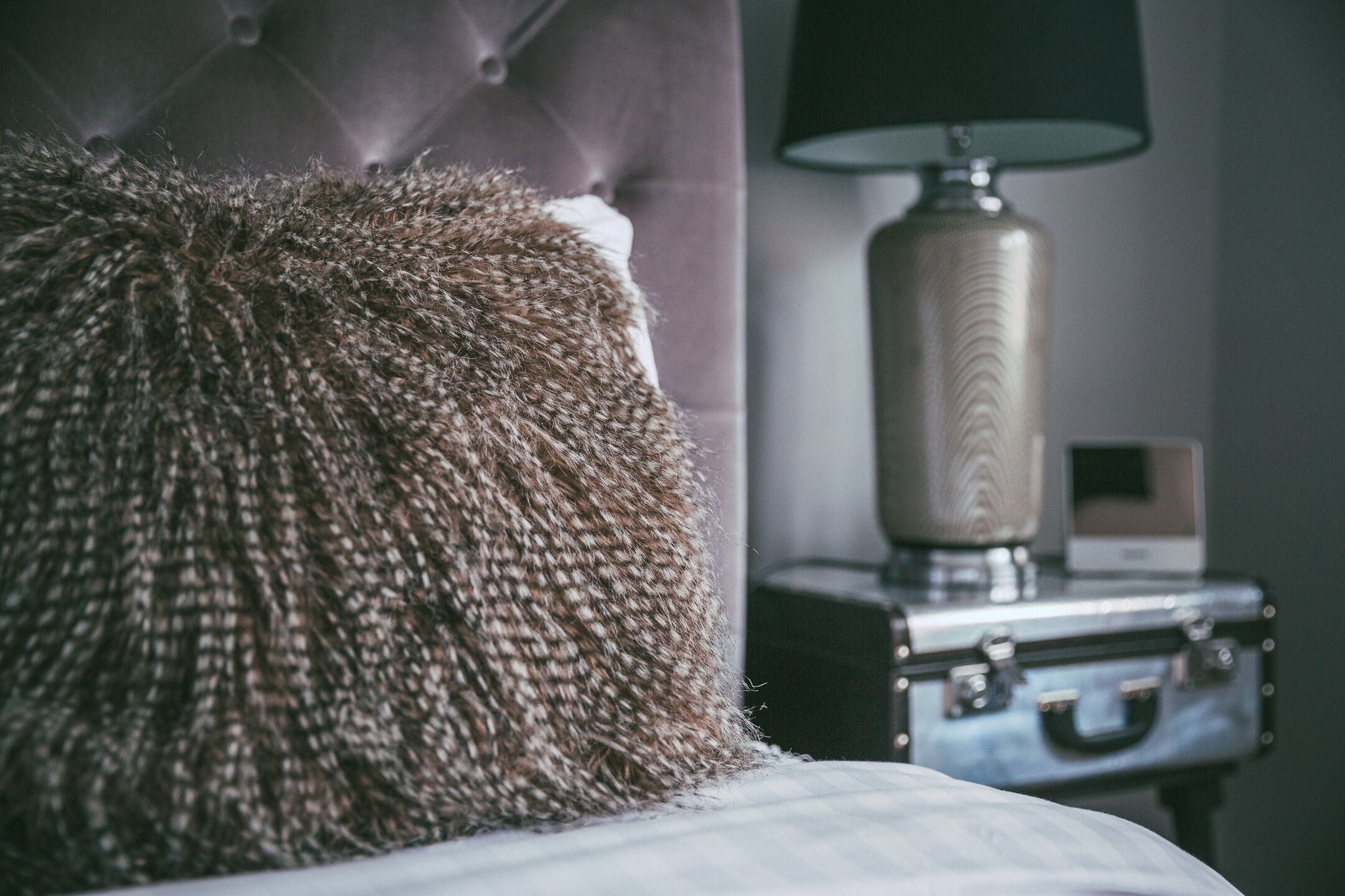 A tufted headboard, a lamp, and a suitcase in a hotel room.