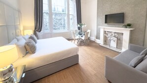 A modern hotel room with a large bed, a sitting area with a sofa and armchairs, a dining table, and a fireplace. - Hanover 71 Suites (Edinburgh)