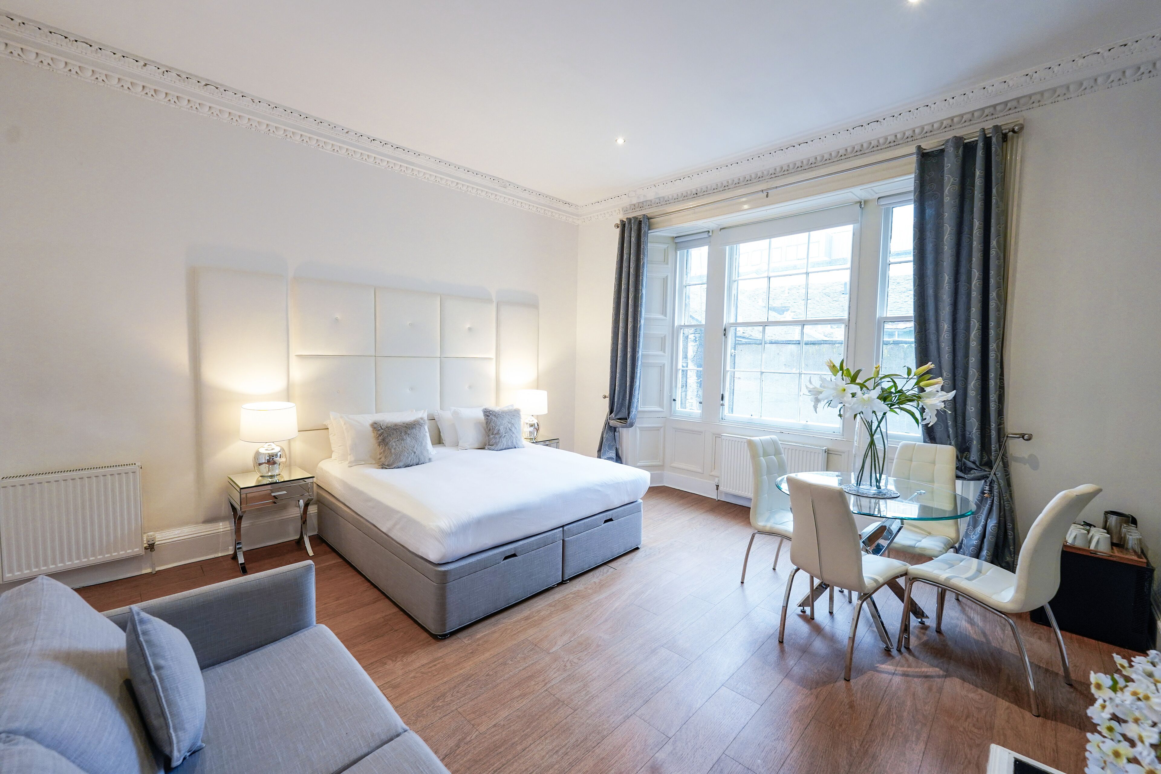 Een moderne slaapkamer met een groot bed, nachtkastjes, een glazen eettafel en een zithoek.