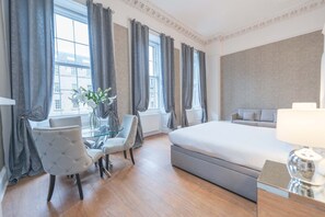 A hotel room with a large bed, a glass table with chairs, and a view of the city through large windows. - Hanover 71 Suites (Edinburgh)