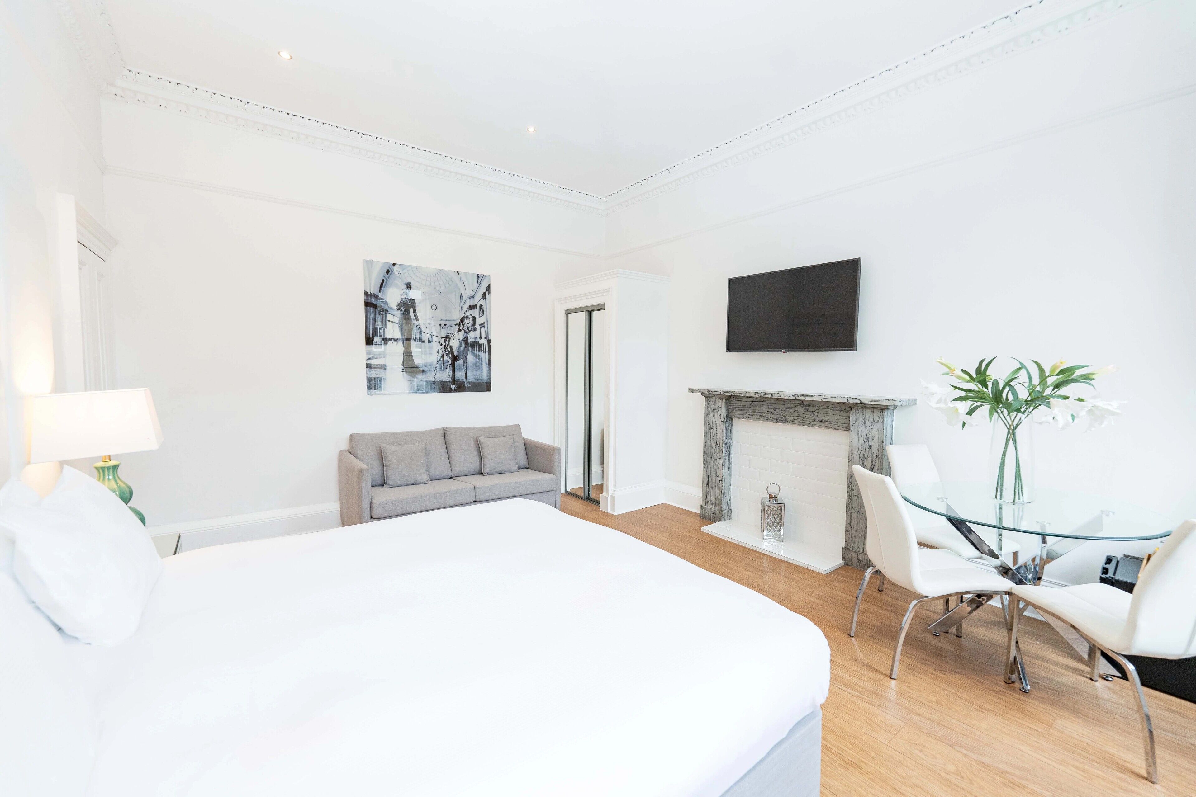 Ein modernes Hotelzimmer mit einem großen Bett, einem grauen Sofa, einem Glastisch mit Stühlen, einem Kamin und einem an der Wand montierten Fernseher.