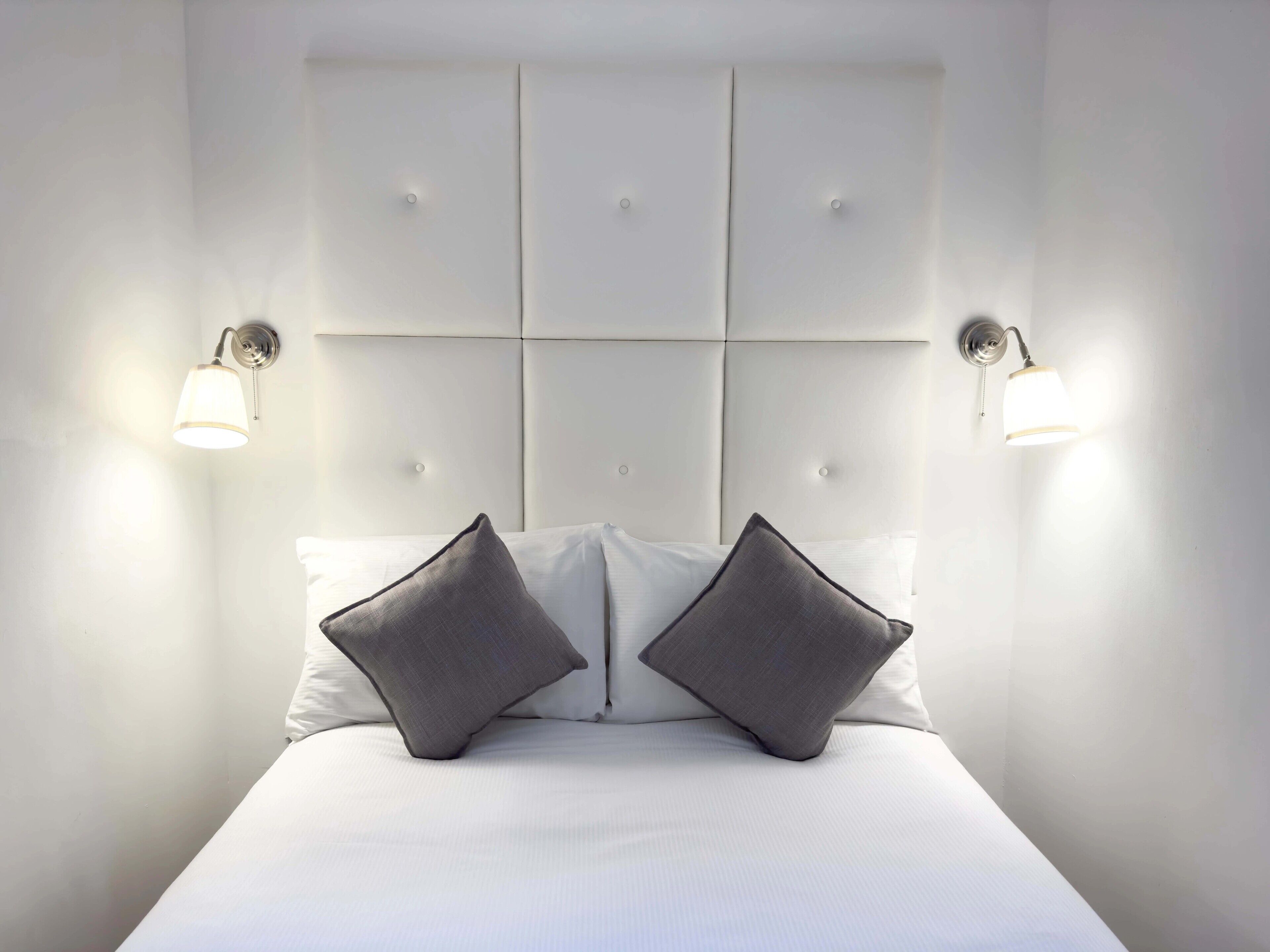 A neatly made bed with a headboard that has a grid pattern and two wall-mounted light fixtures on either side.