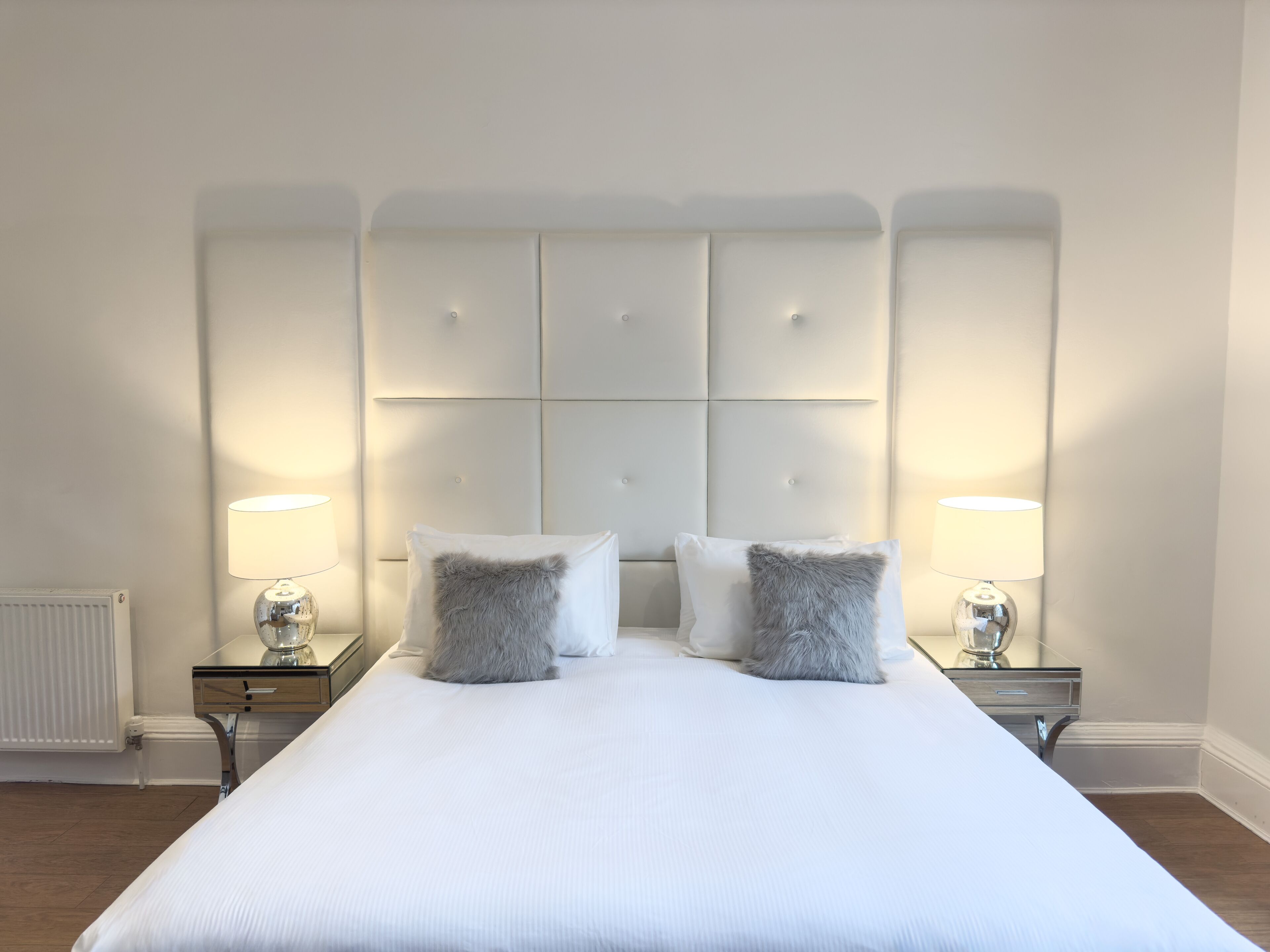 Una cama grande con cabecera capitonada, dos lámparas de noche y dos almohadas mullidas.