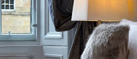 Une pièce avec une fenêtre, une lampe et un plaid en fourrure sur le lit.