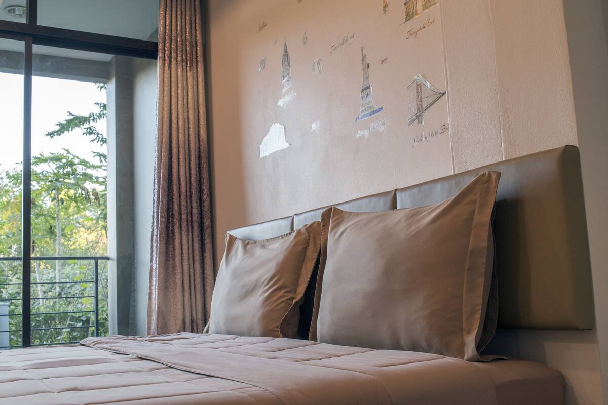 A neatly made bed with a headboard, a window with a view of trees, and a wall with a map.