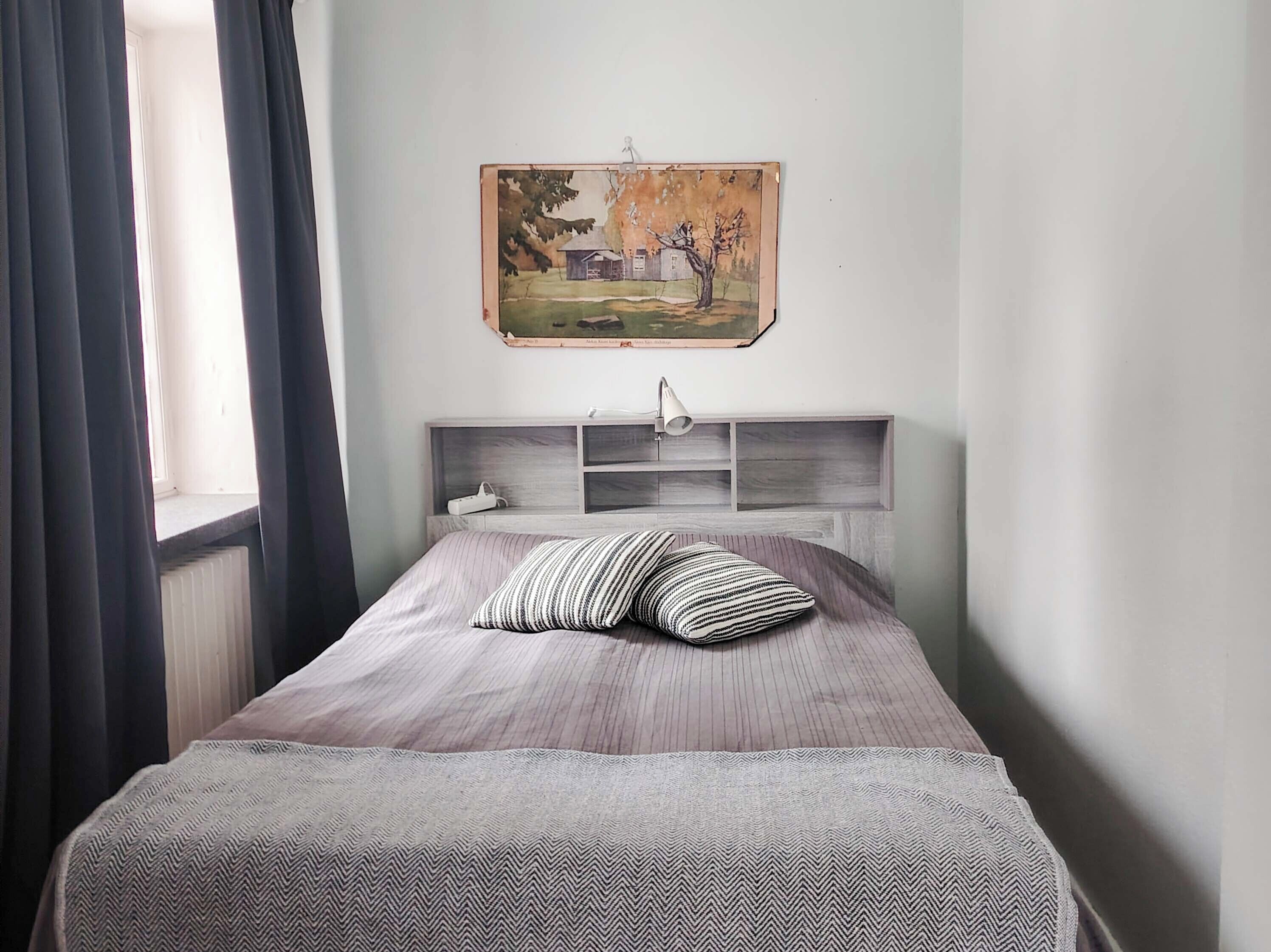 Ein Schlafzimmer mit einem Bett, einem Kopfteil mit Ablagen, einem Gemälde und einem Fenster mit Vorhängen.