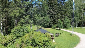 A serene outdoor area with picnic tables and a covered seating area surrounded by dense greenery and trees. - Vanhan Koulun Majatalo (Lieksa)