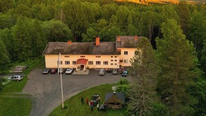 A two-story building with a parking area in front, surrounded by dense forest. - Vanhan Koulun Majatalo (Lieksa)