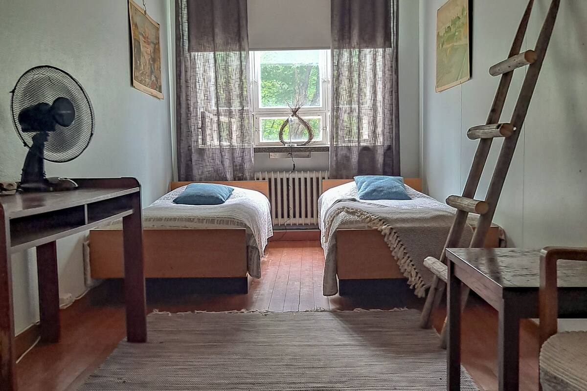A room with two beds, a radiator, a fan, and a ladder.