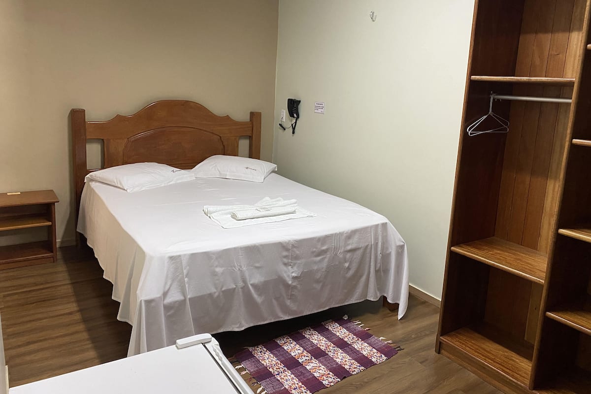 A neatly made bed with white linens, a wooden headboard, and a small bedside table.