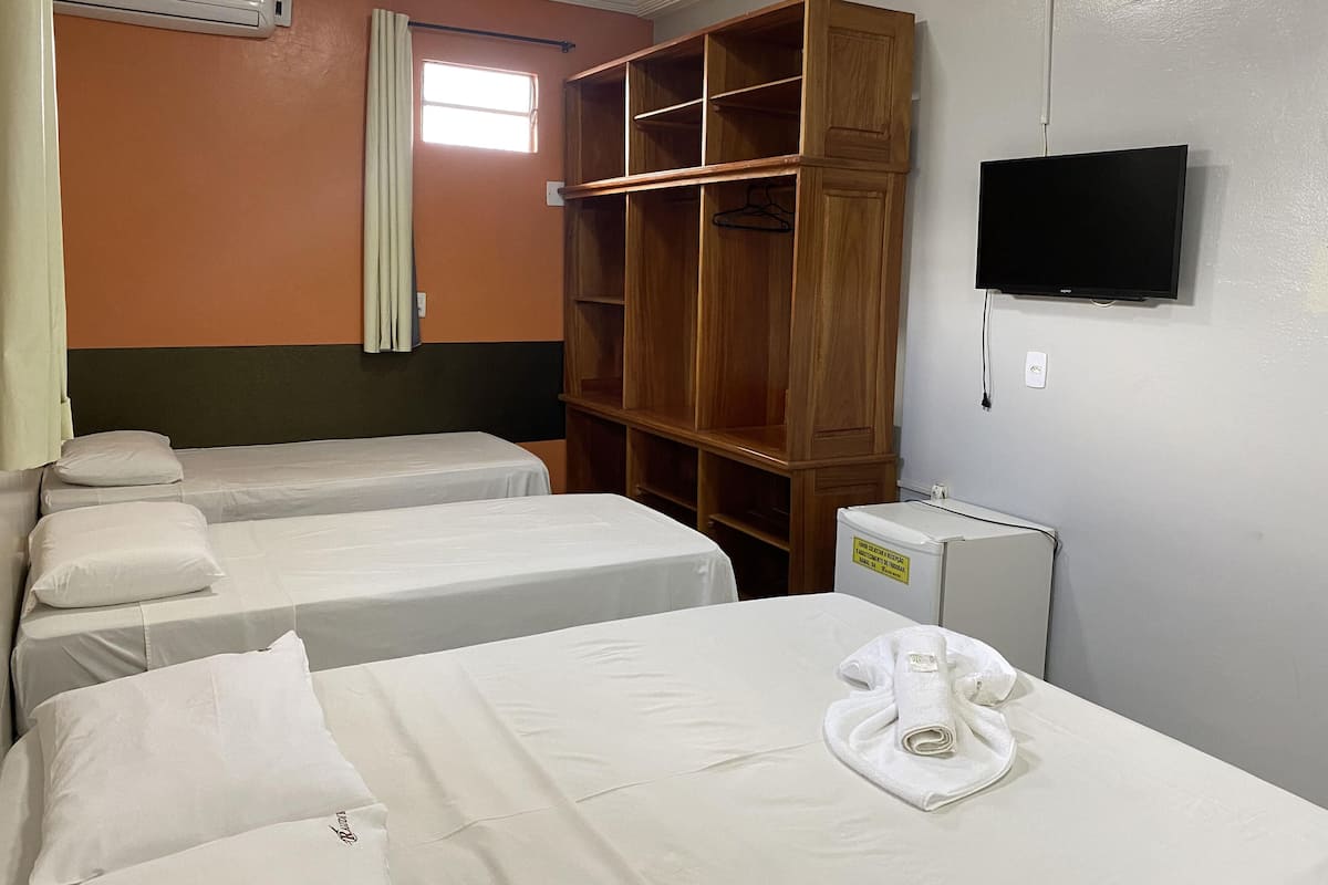 A hotel room with two single beds, a wooden wardrobe, a TV, and an air conditioning unit.