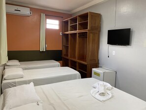 A hotel room with two single beds, a wooden wardrobe, a TV, and an air conditioning unit.