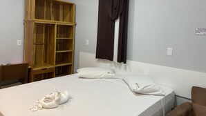 Una habitación de hotel con cama, un armario de madera, una ventana con cortinas y un equipo de aire acondicionado.