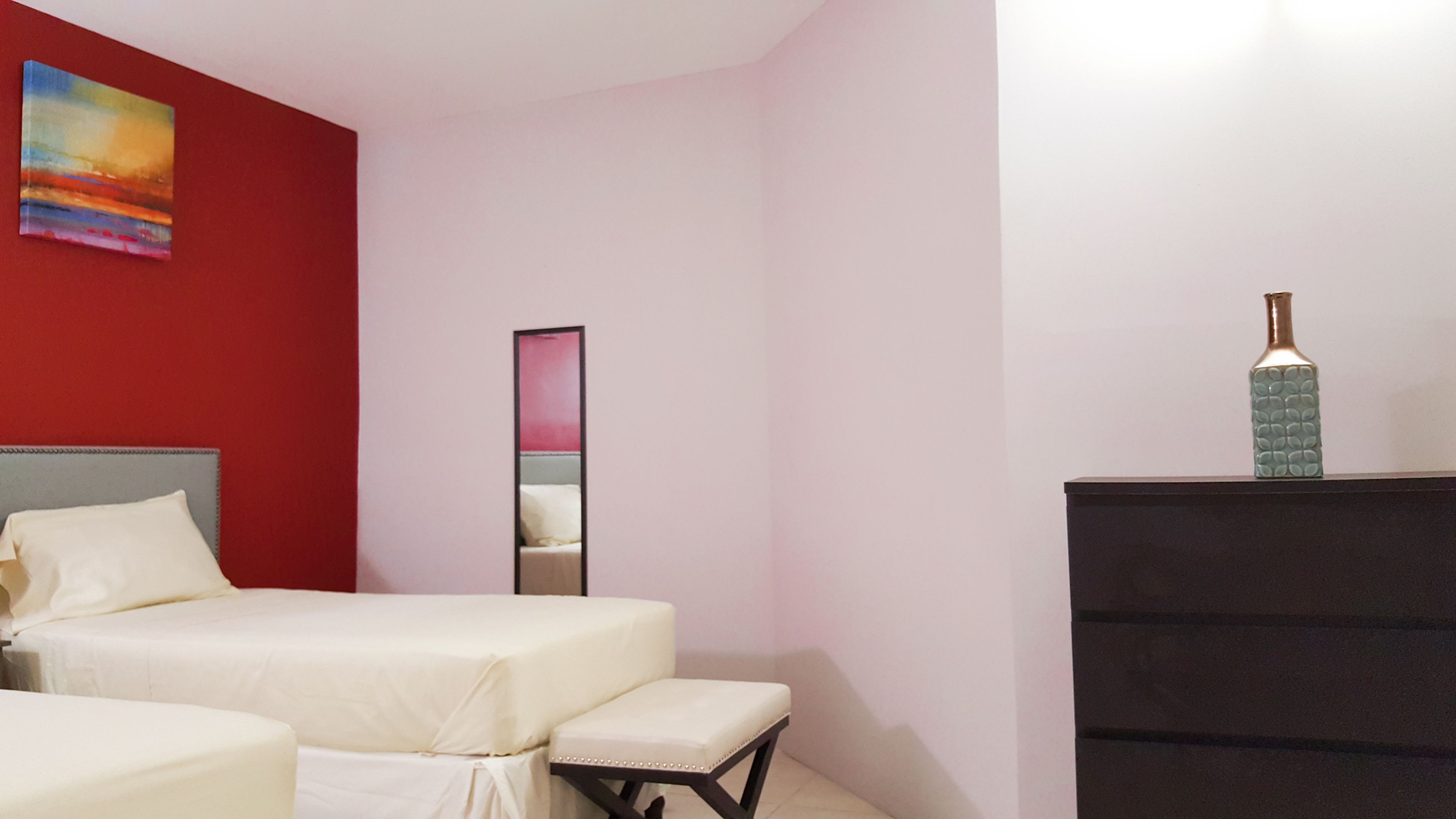 Une chambre d’hôtel avec deux lits, une commode, un miroir et un vase décoratif.